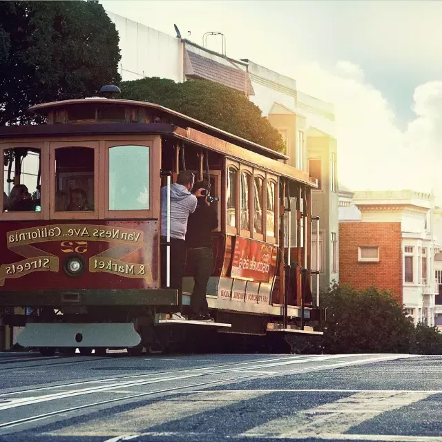 Un teleférico rodea una colina en San Francisco con pasajeros mirando por la ventana.